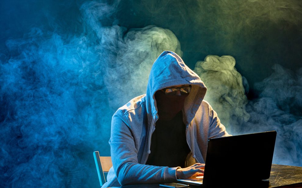 Hooded computer hacker stealing information with laptop